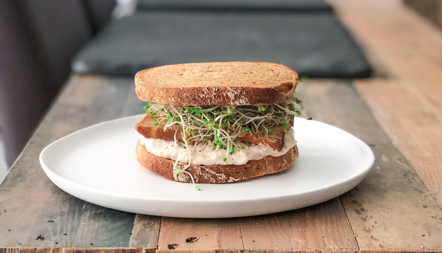 The Cannellini Miso Mash Sandwhich overflowing with sprouts on wood dining table